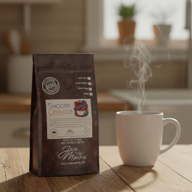 A bag of Smooth Operator Mixed Roast Blend | Low Acid Coffee rests on a wooden table beside a steaming white mug, set against the backdrop of a cozy kitchen.